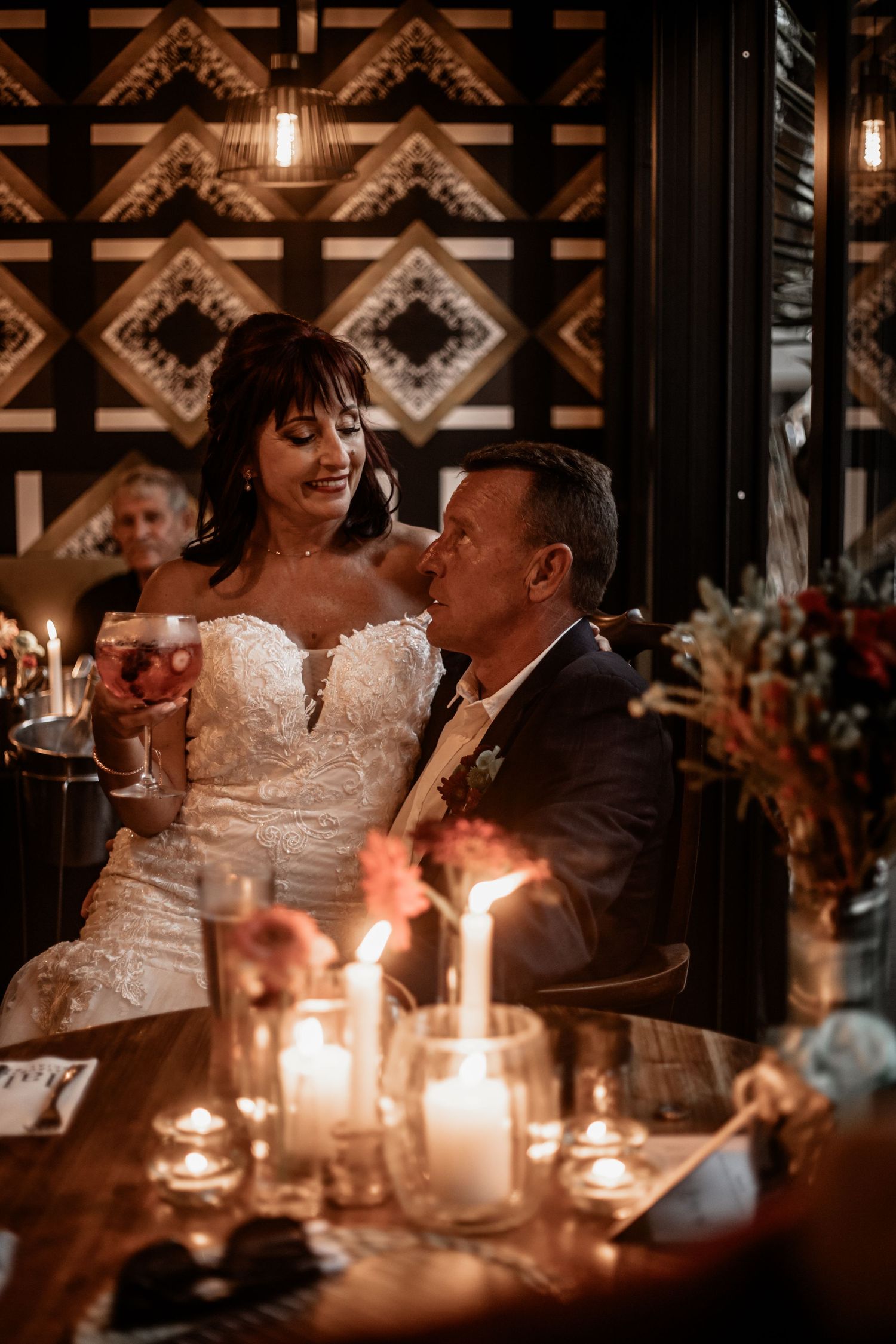 Romantic candlelit wedding reception with ornate geometric wall decor and glowing ambient lighting at an intimate venue.
