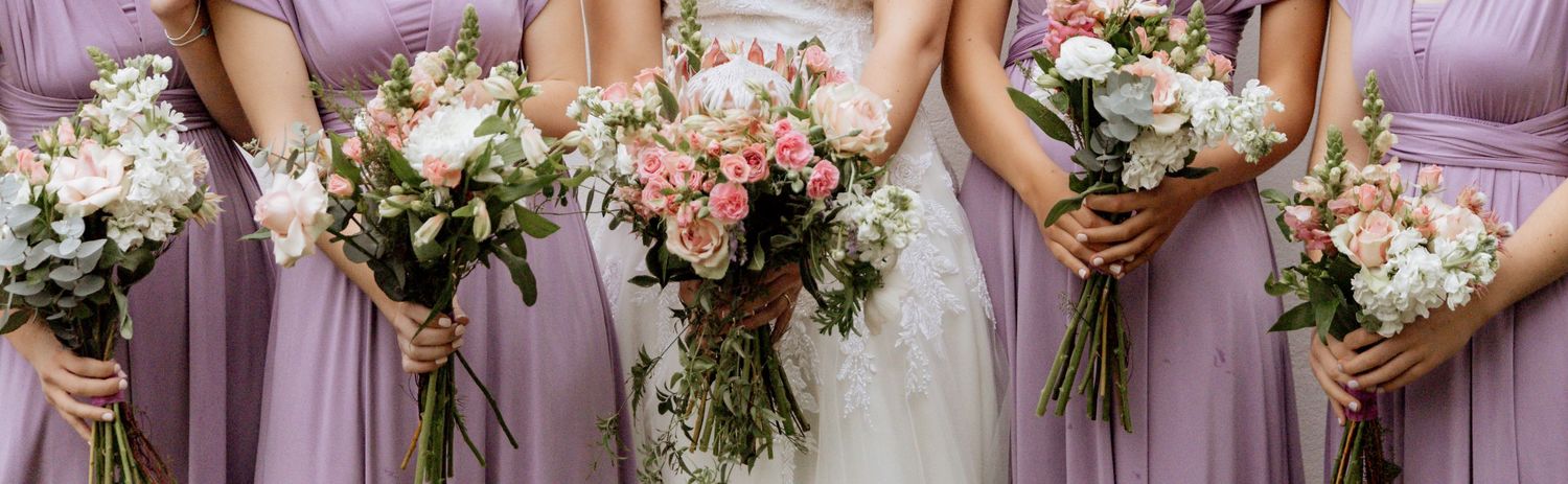 Elegant wedding party wearing mauve bridesmaid dresses hold lush white and pink floral bouquets.