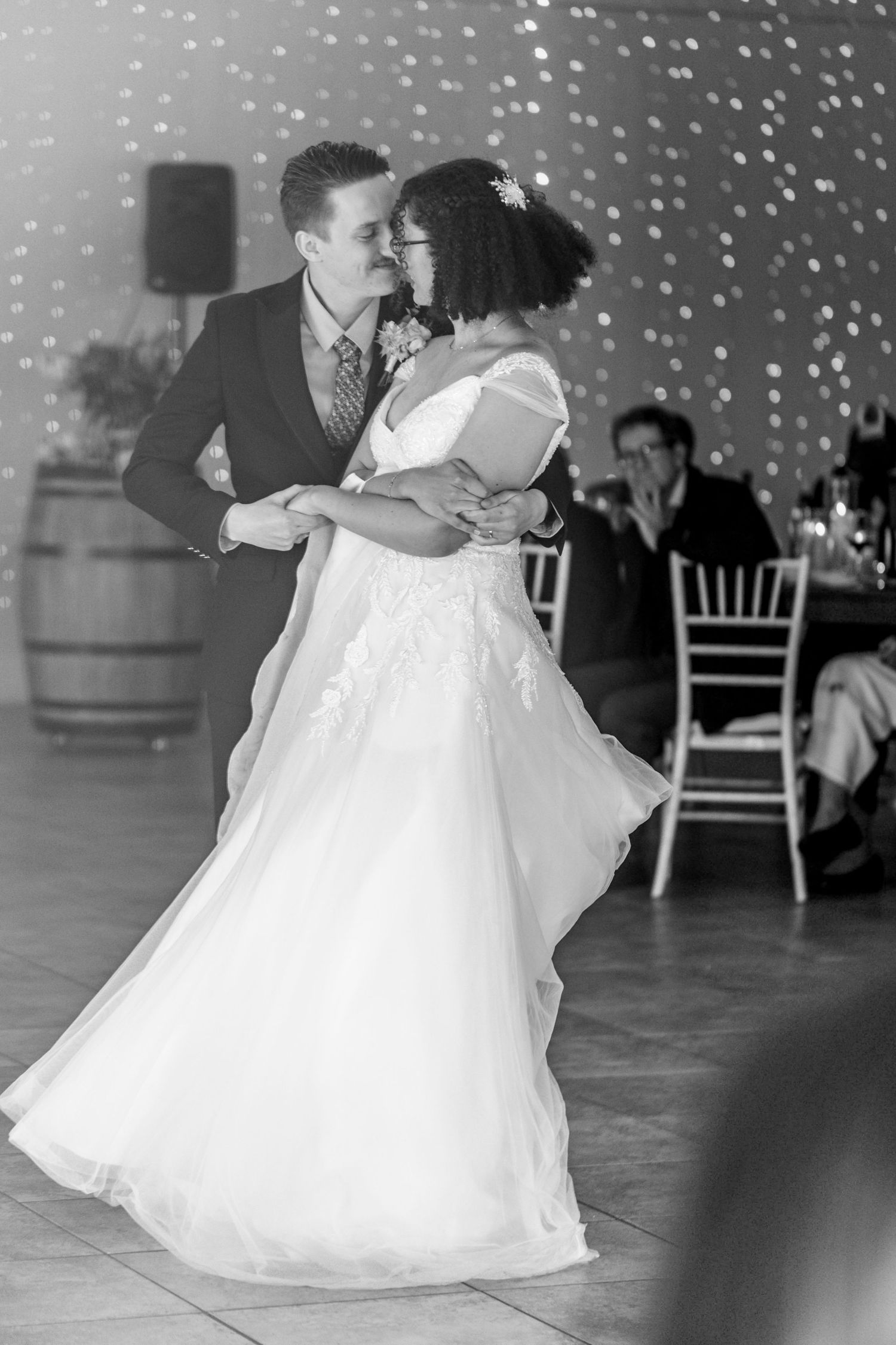 A couple shares their first dance at a wedding reception with string lights twinkling in the background.