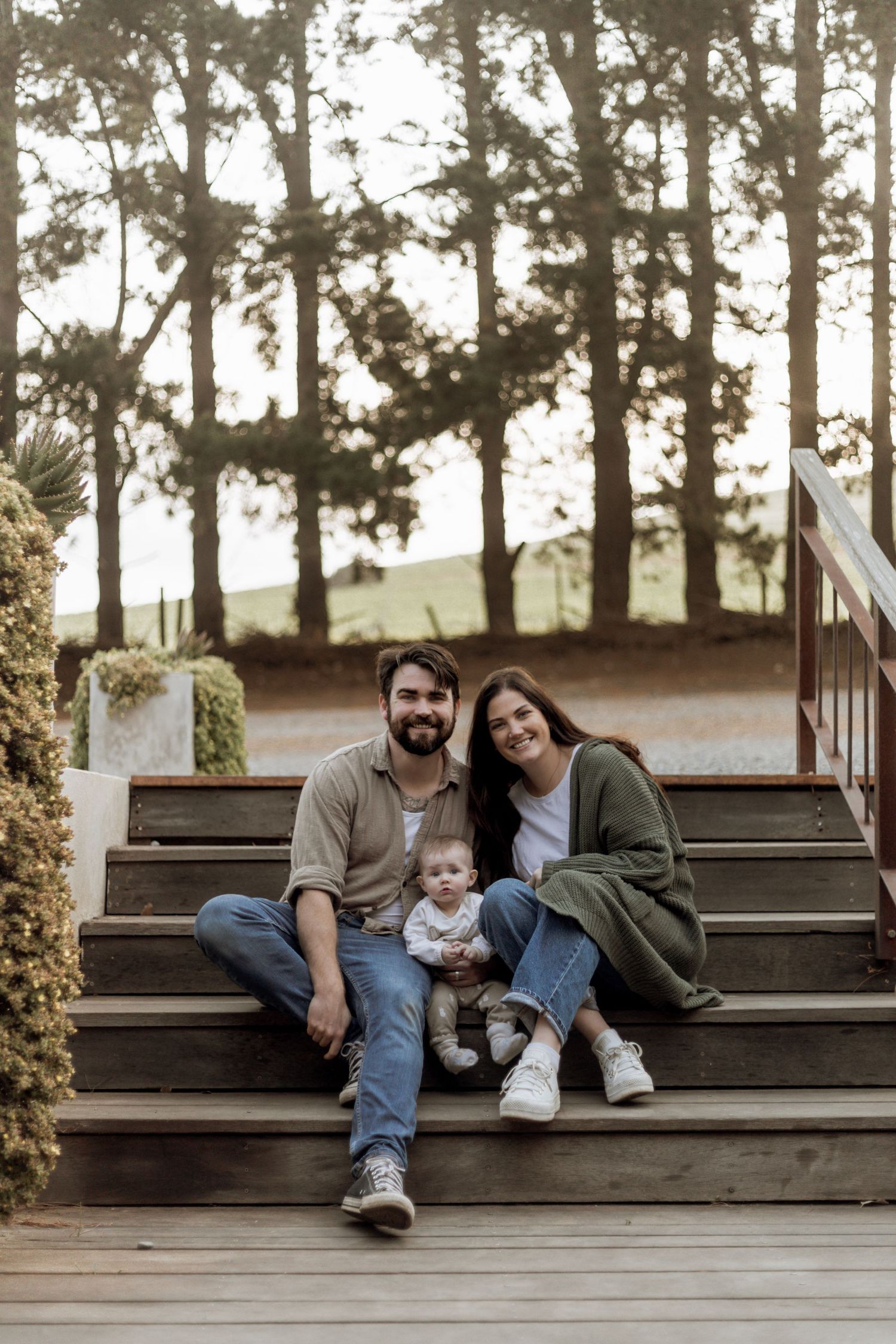A family sits together on wooden steps in a wooded outdoor setting during a photo session.