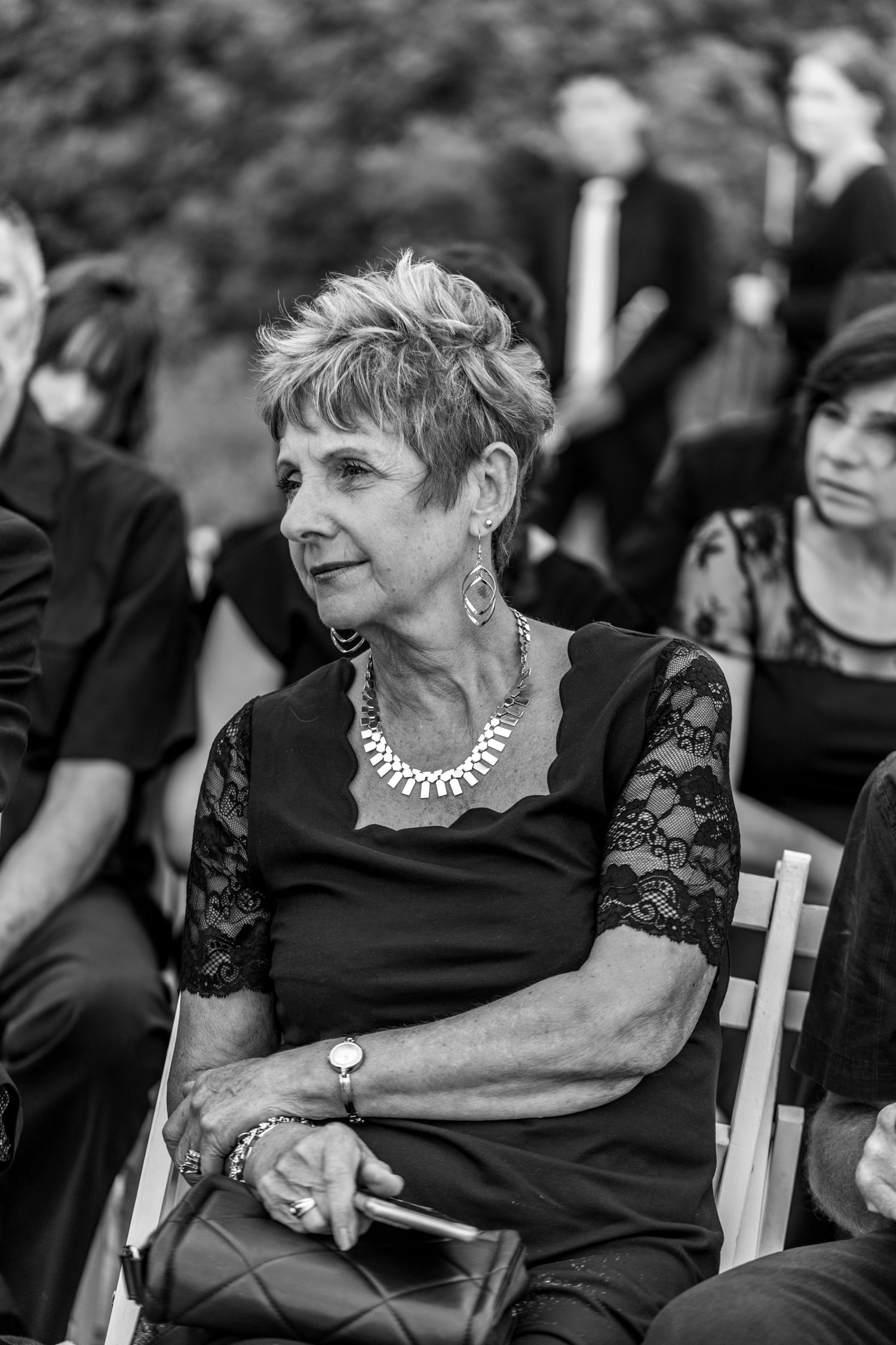 Black and white photo of a woman in lace dress and pearl necklace sitting in a chair at a formal event.