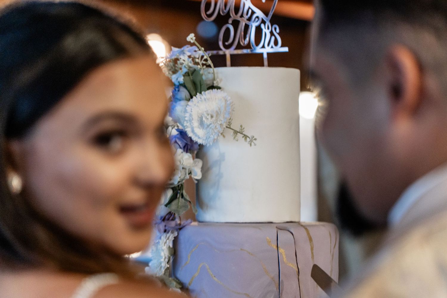 A contemporary wedding cake decorated with blue flowers and silvery accents stands elegantly at a celebration.