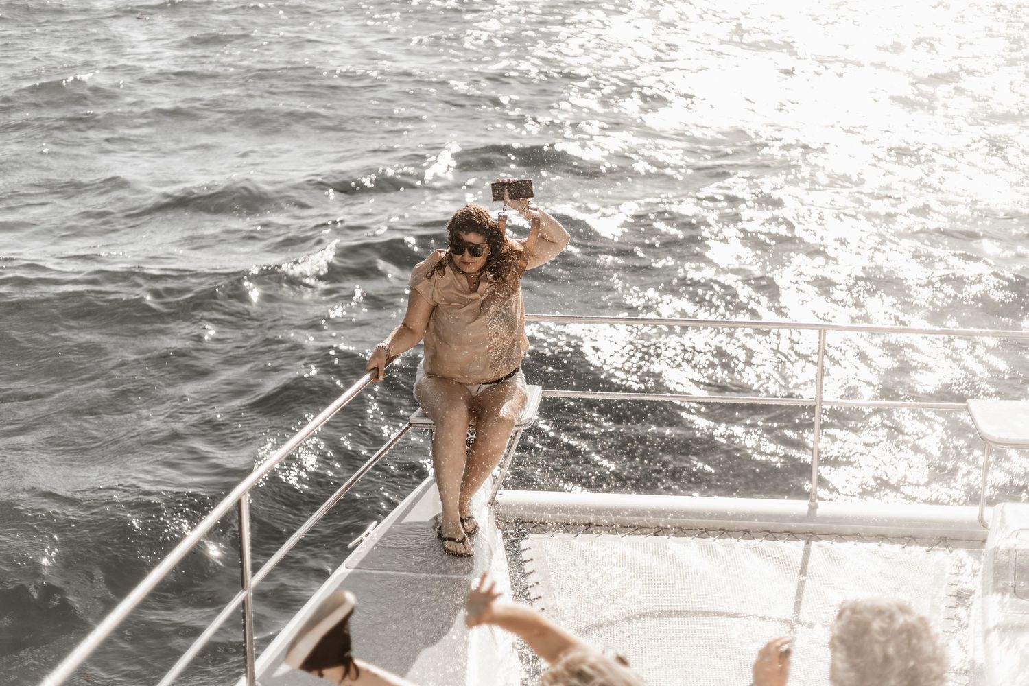 A person stands on the edge of a boat deck overlooking the sparkling ocean waves on a sunny day.