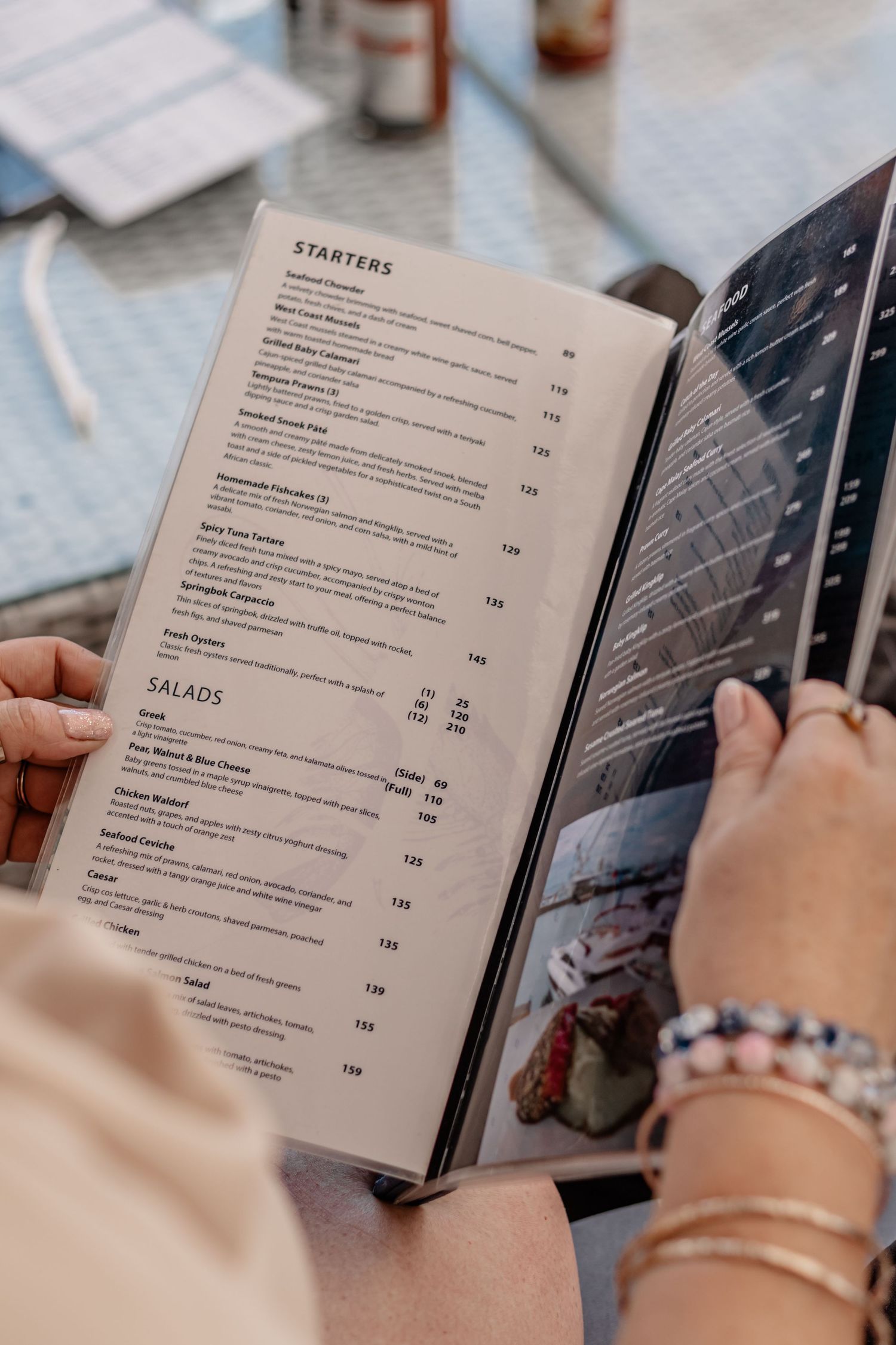 Someone holding a restaurant menu open to the starters and salads sections while dining at a restaurant.