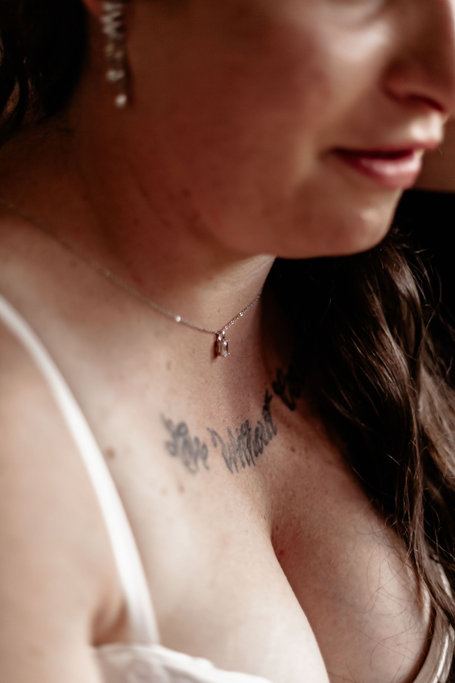 Close-up view of a neck area showing glimpses of a tattoo and necklace with soft lighting.