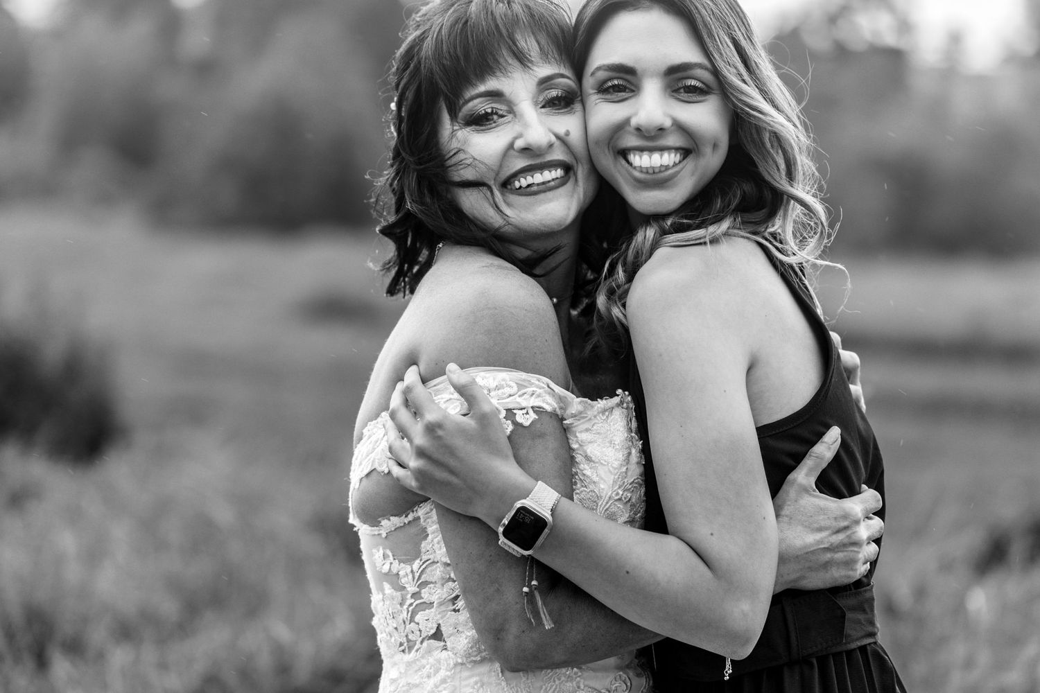 Two people embrace and smile joyfully while posing outdoors in a black and white photograph.