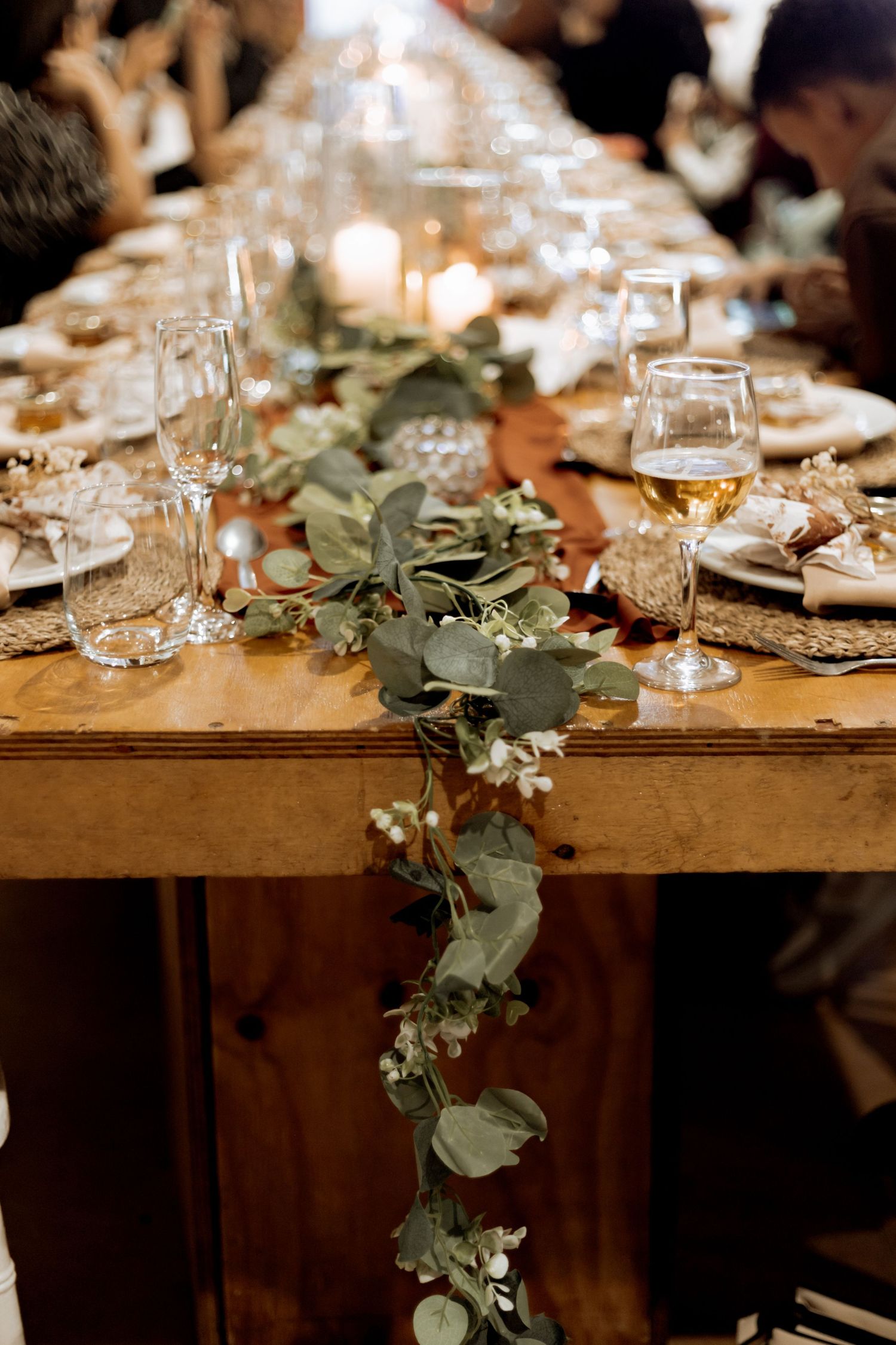 Rustic wooden dining table decorated with eucalyptus garland and elegant wine glasses for an intimate gathering.