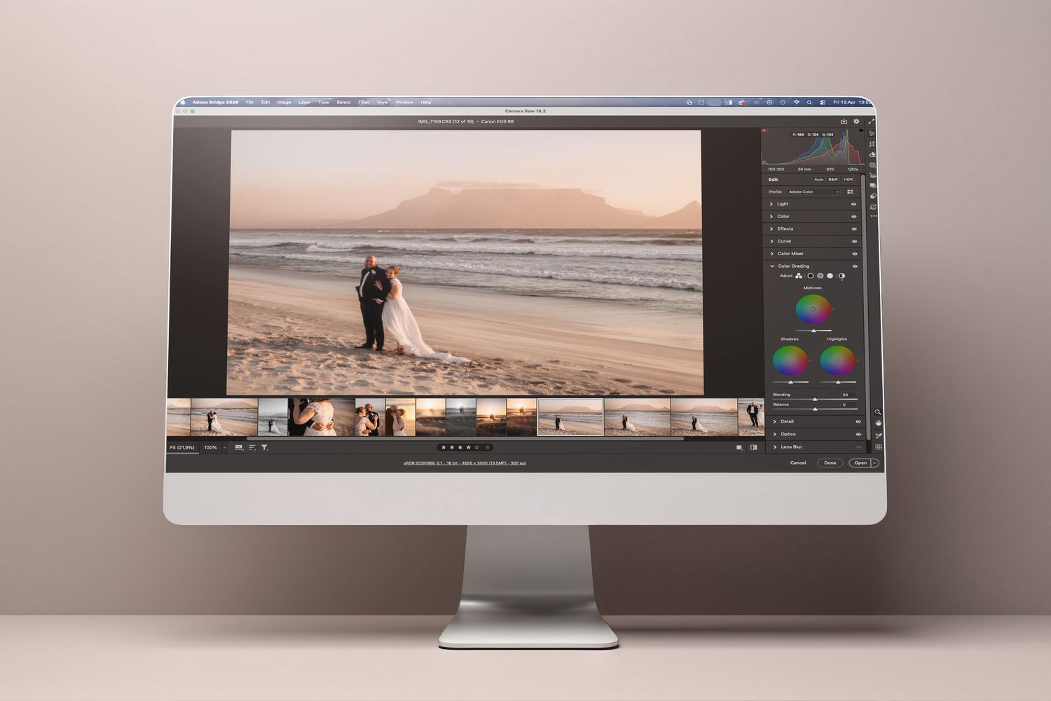iMac displaying wedding photo editing in Lightroom, showing couple on beach with mountain backdrop.