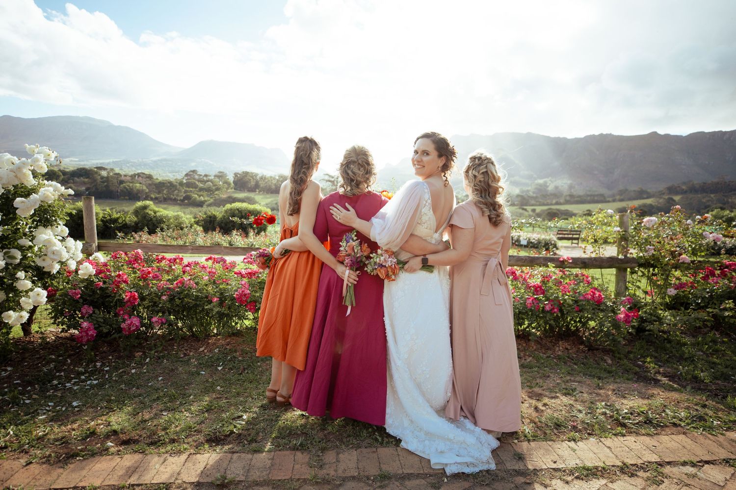 Wedding party members stand together in a garden overlooking mountains and vineyards on a sunny afternoon.