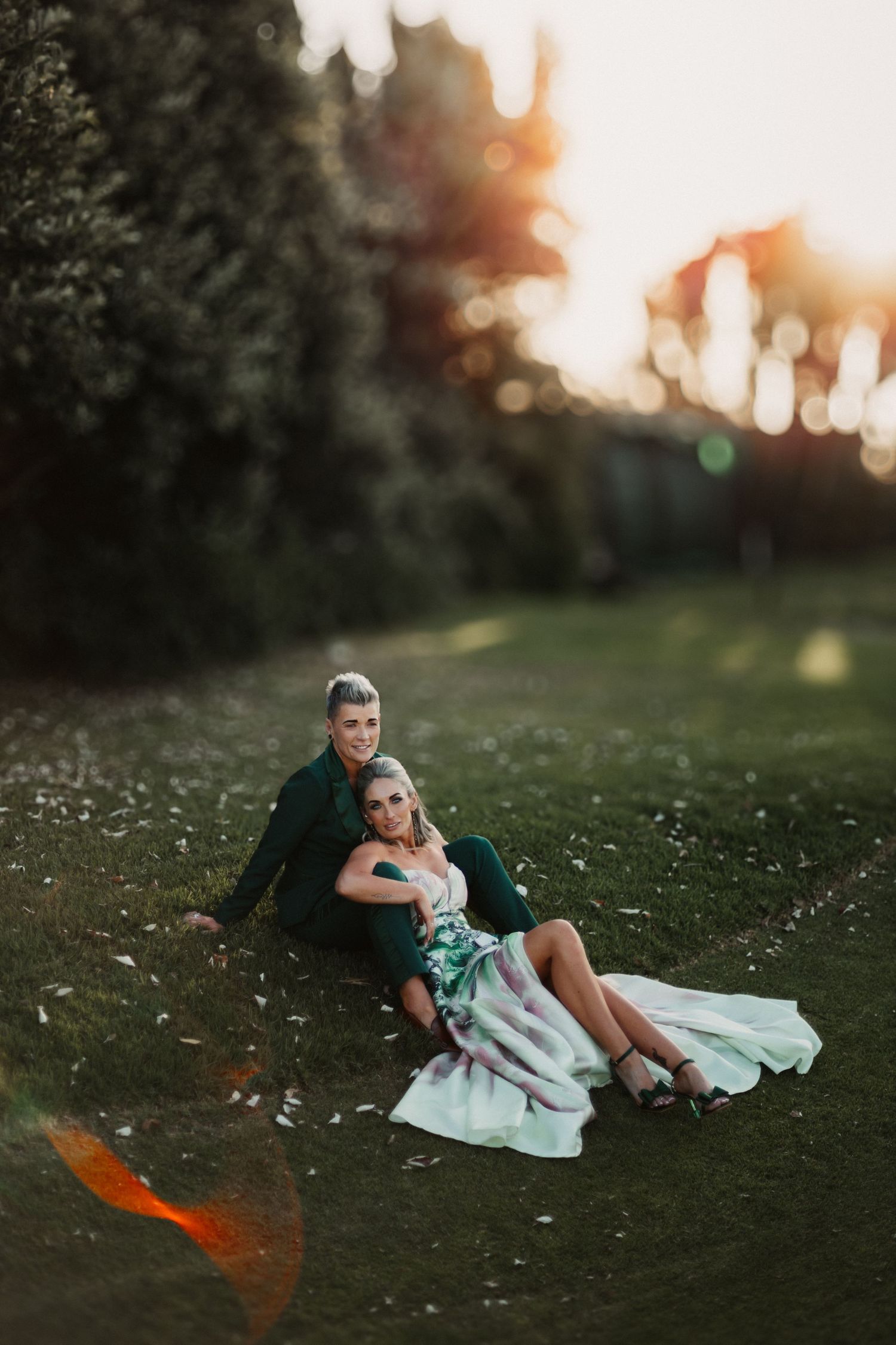 A romantic sunset photo shoot in a grassy field with soft golden light and scattered white flowers.