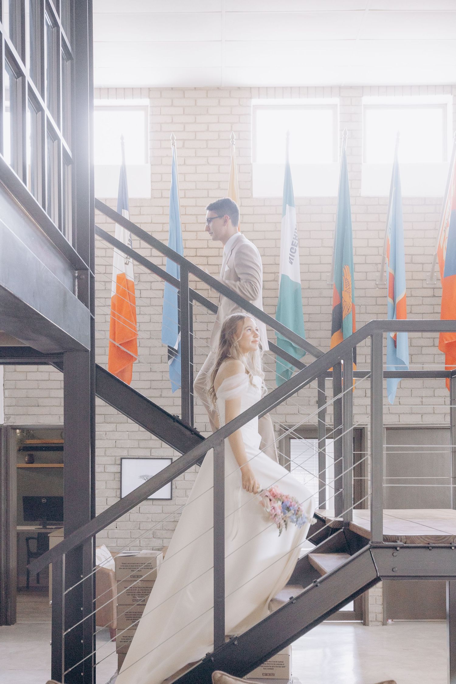 A figure in a flowing white dress descends a modern black staircase in a series of graceful steps.