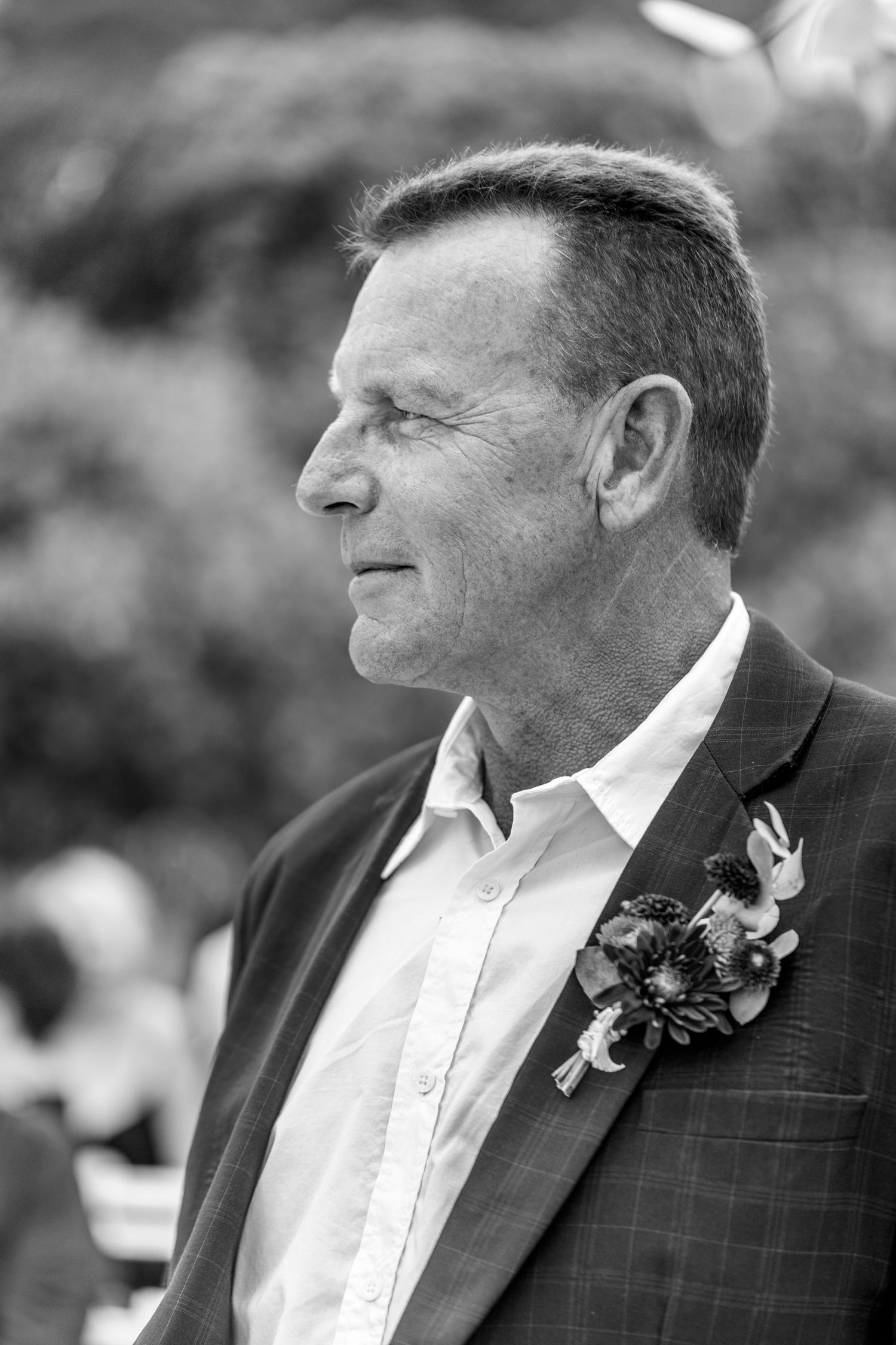 Black and white profile portrait of smiling wedding guest wearing suit jacket with boutonniere.