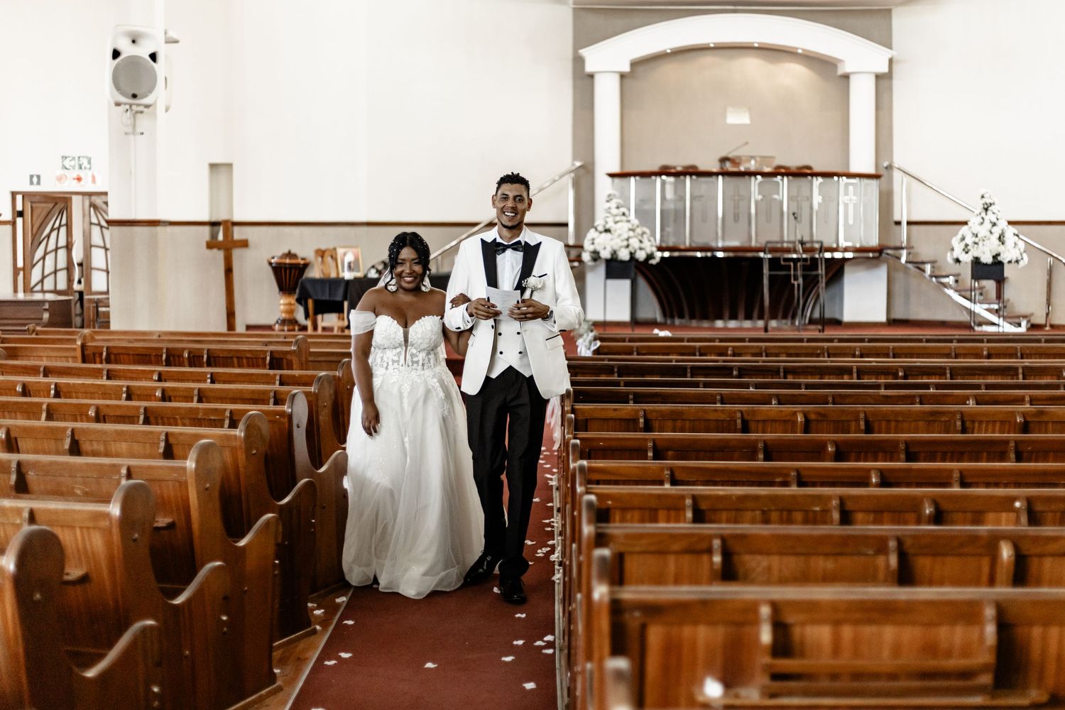 A wedding party in formal attire walks down the church aisle from different angles during a traditional ceremony.