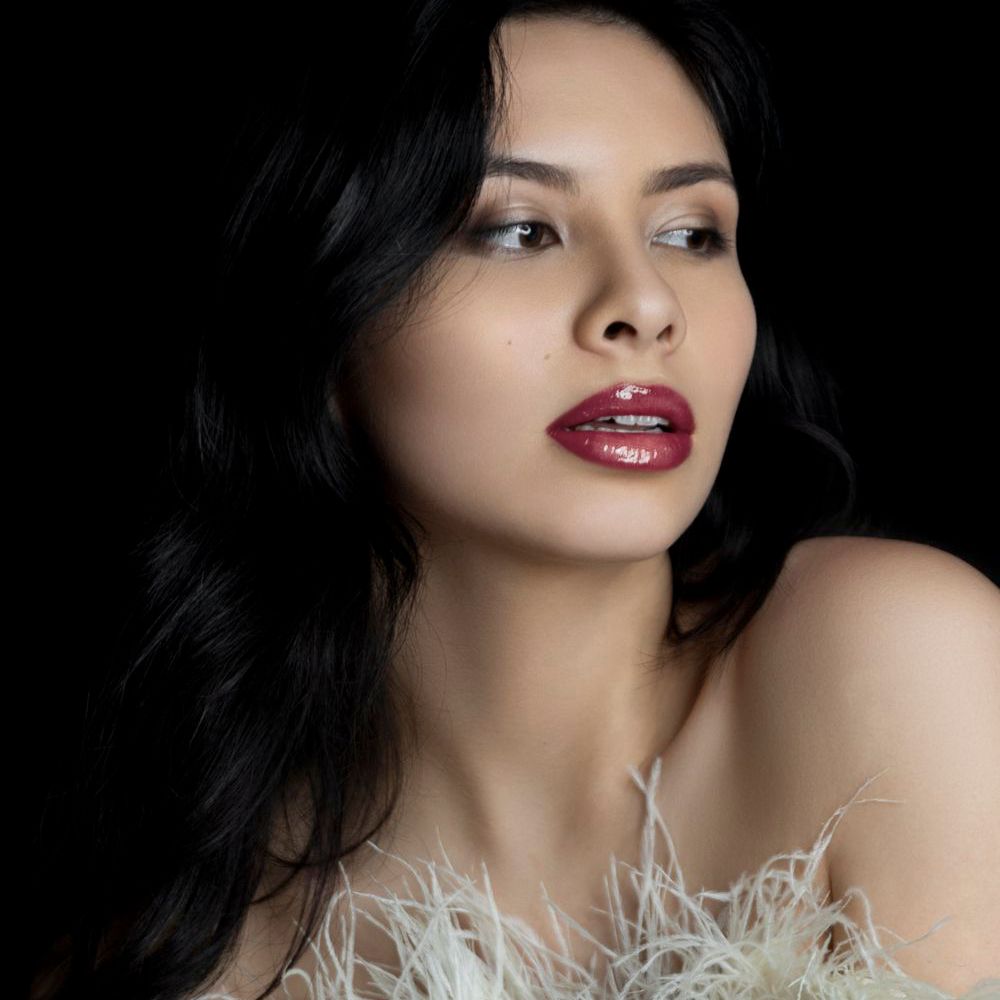Beauty portrait featuring dramatic red lipstick and feathered white garment against dark background.