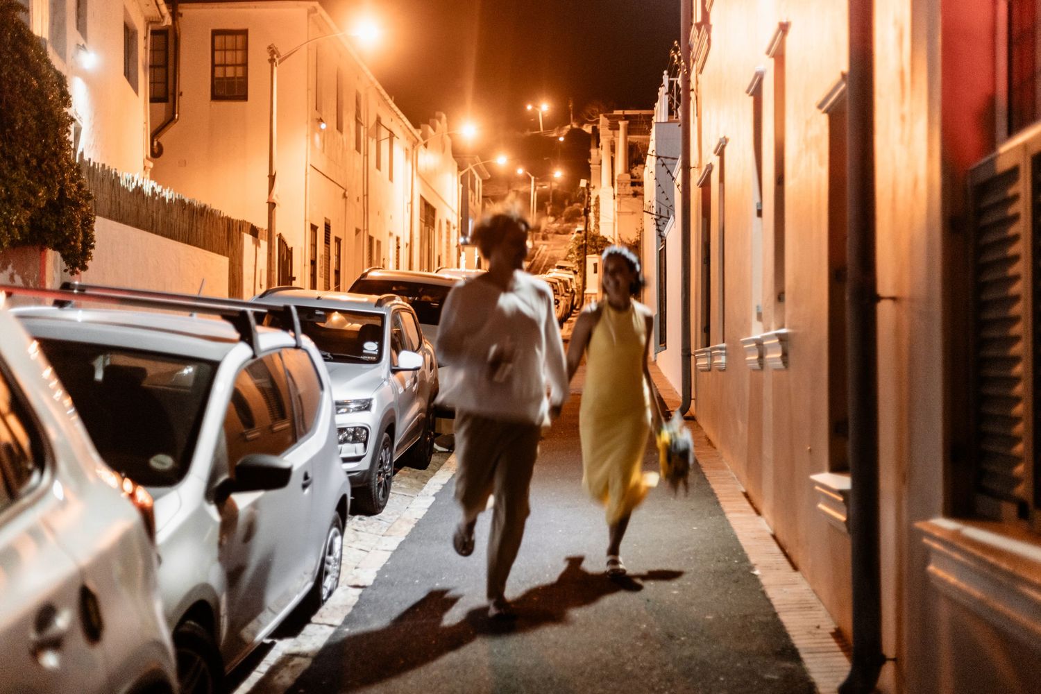 Street performers dance and leap through a narrow alley illuminated by warm streetlights in an urban setting.