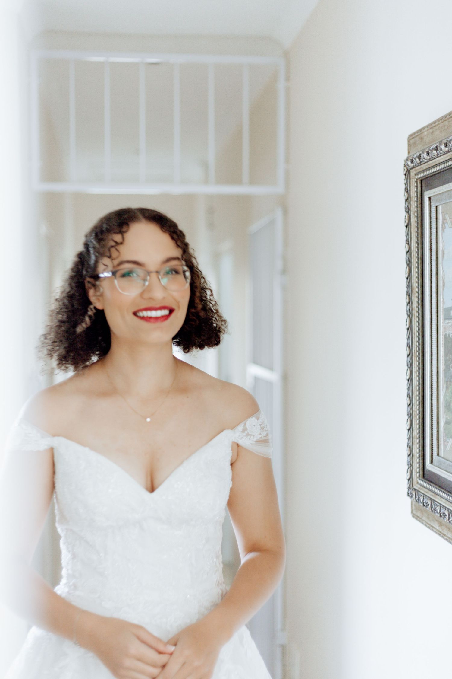 Glowing bride in a white lace wedding dress and glasses smiles radiantly in a series of candid getting-ready photos.