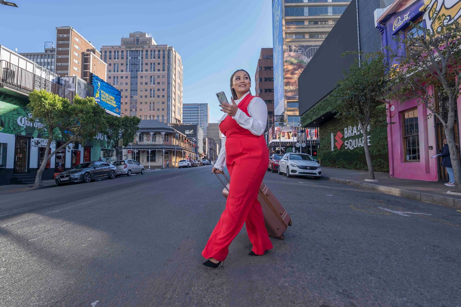 A person in a bright red jumpsuit poses playfully in the middle of an urban street with tall buildings in the background.