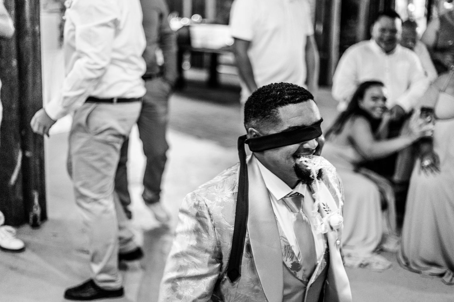 A person in sunglasses and a vest walks confidently down a black and white street scene with people in the background.