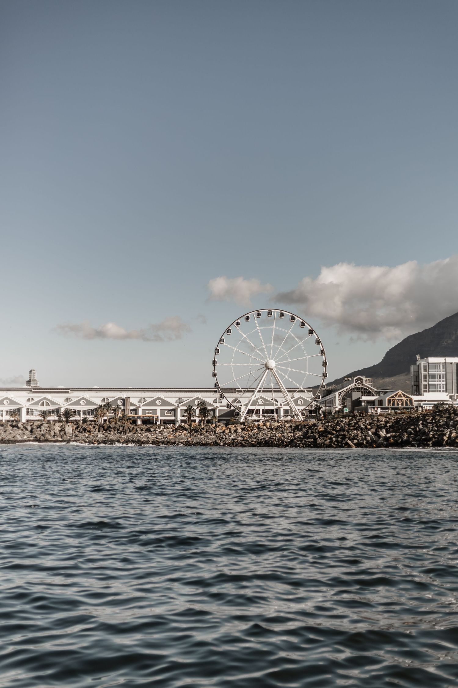A scenic panoramic view of a seaside pier with a large Ferris wheel taken from the ocean perspective at twilight.
