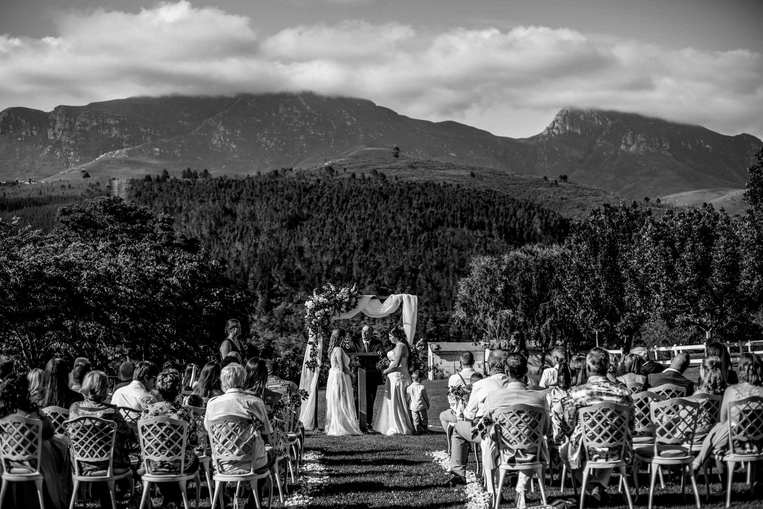 Black and white mountain landscape panorama with trees and people gathered for an outdoor wedding ceremony.