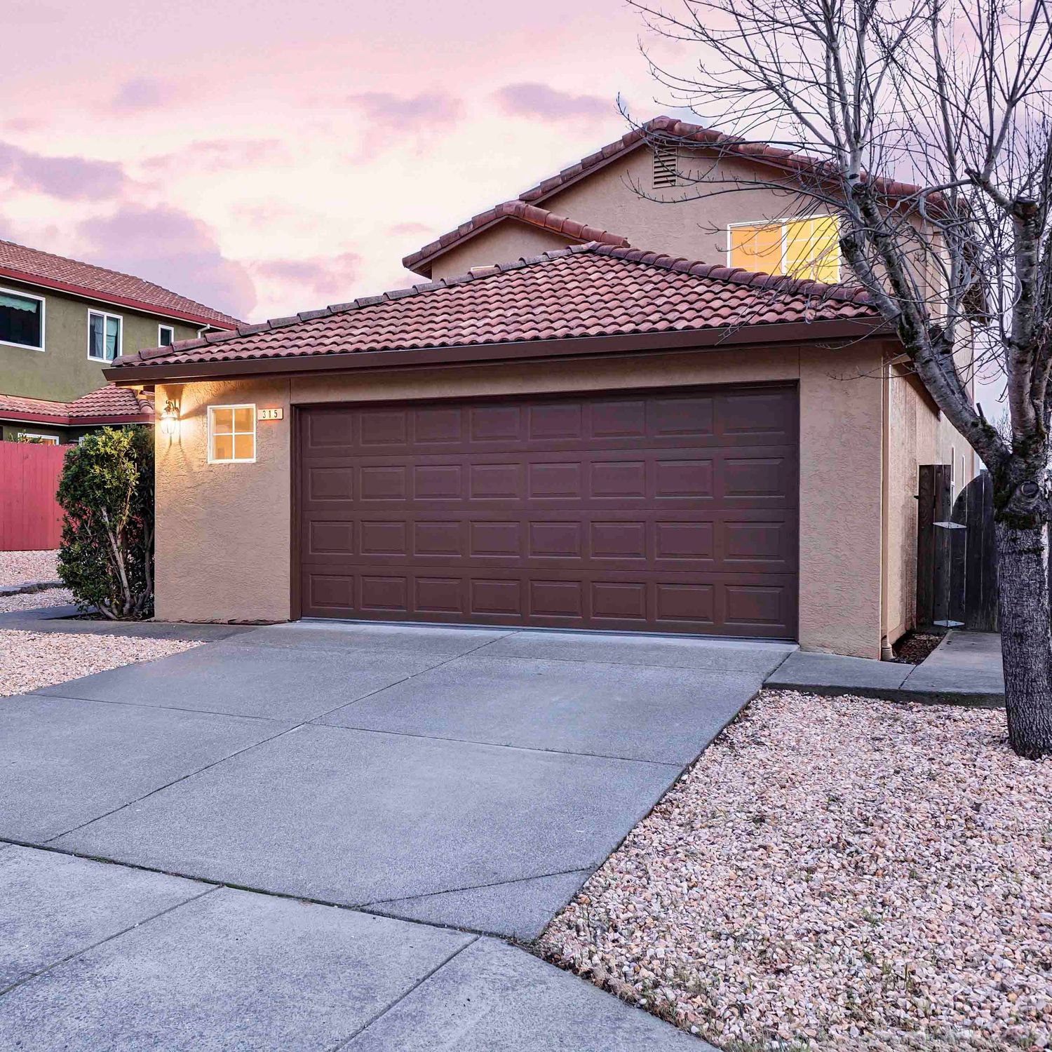 Suburban home exterior with concrete driveway and desert xeriscaping at sunset.