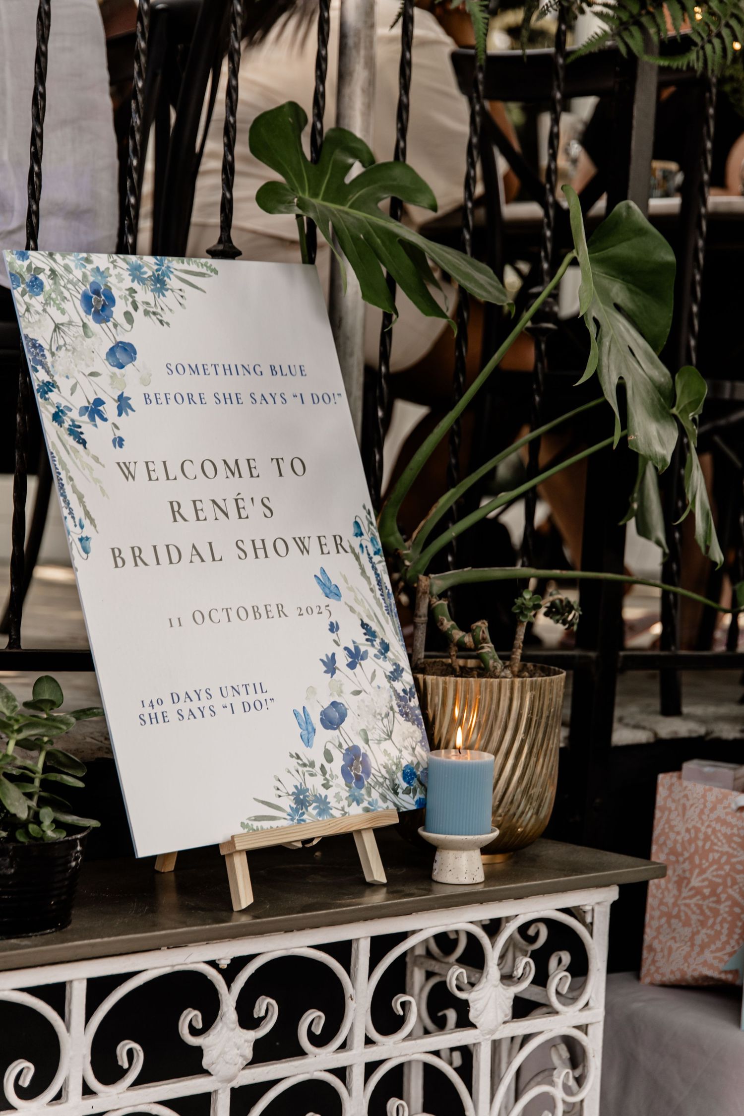 Blue floral bridal shower welcome sign on easel for Rene's October wedding celebration with candle decor.