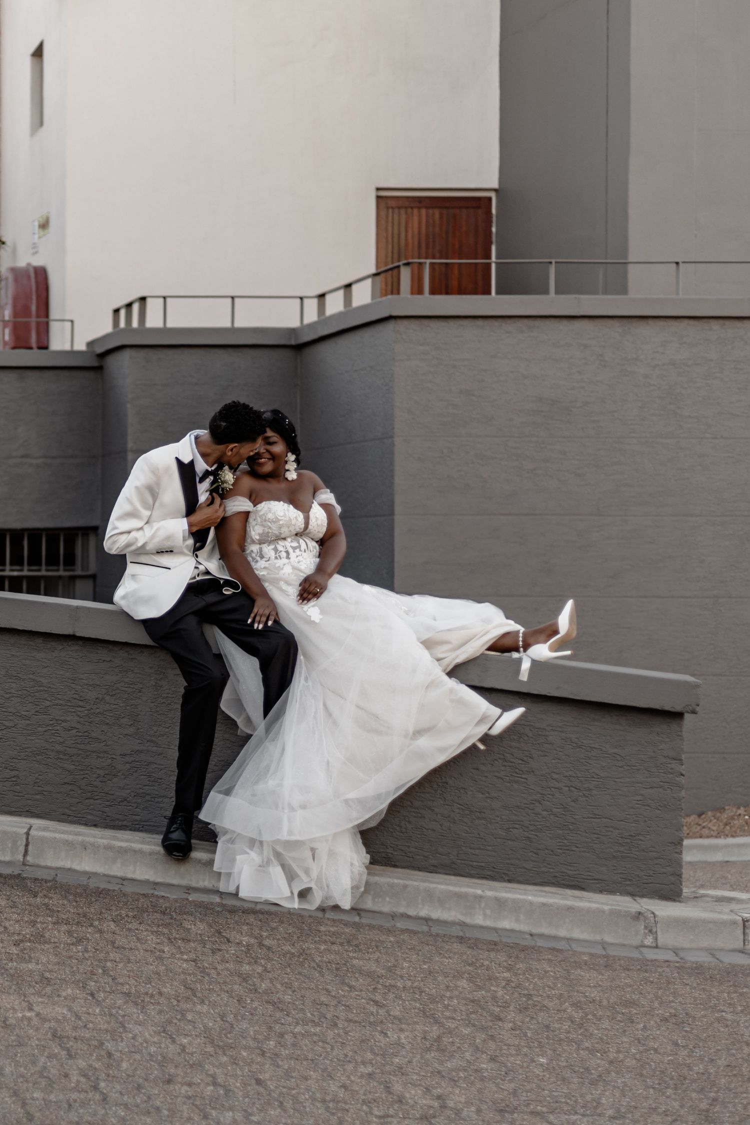 Newlywed couple shares a romantic dip pose against a grey wall in formal wedding attire.