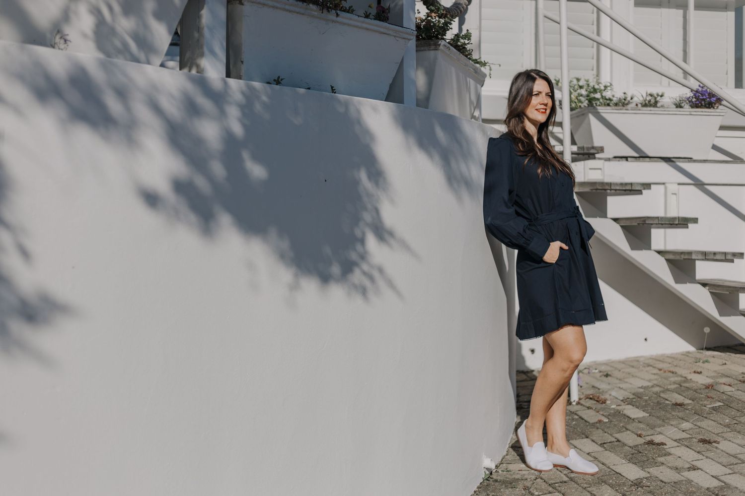 A woman in a flowing navy dress poses on a cascading flight of concrete steps in a modern outdoor setting.