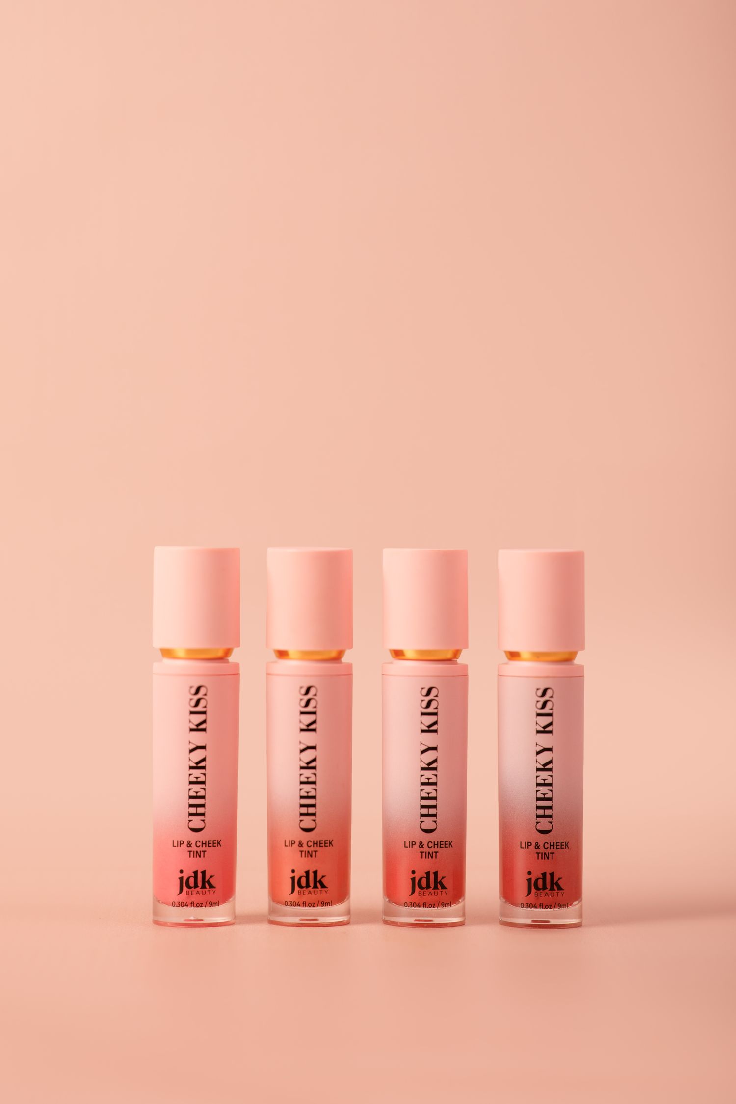 Four pink cosmetic product bottles arranged in a row on a pink background with soft lighting and minimalist styling.