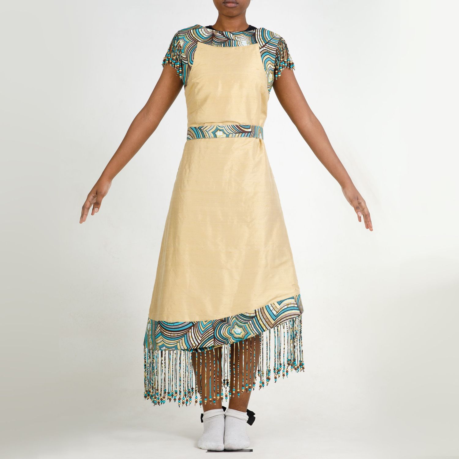 Native American dress in cream color with detailed turquoise trim and beaded fringe detail, displayed on mannequin.