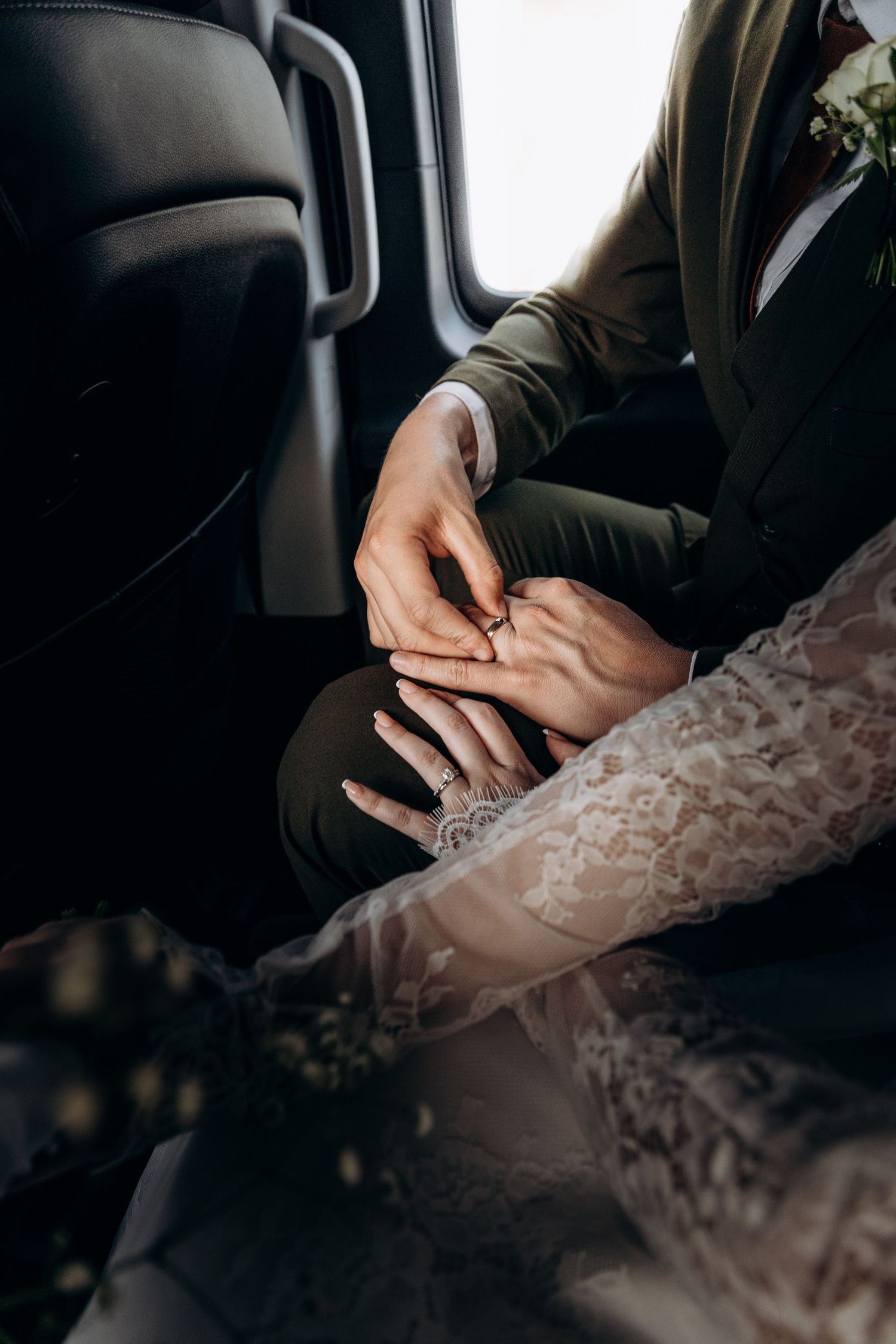 Bride and groom exchanging rings in a car, close-up of hands in wedding attire.