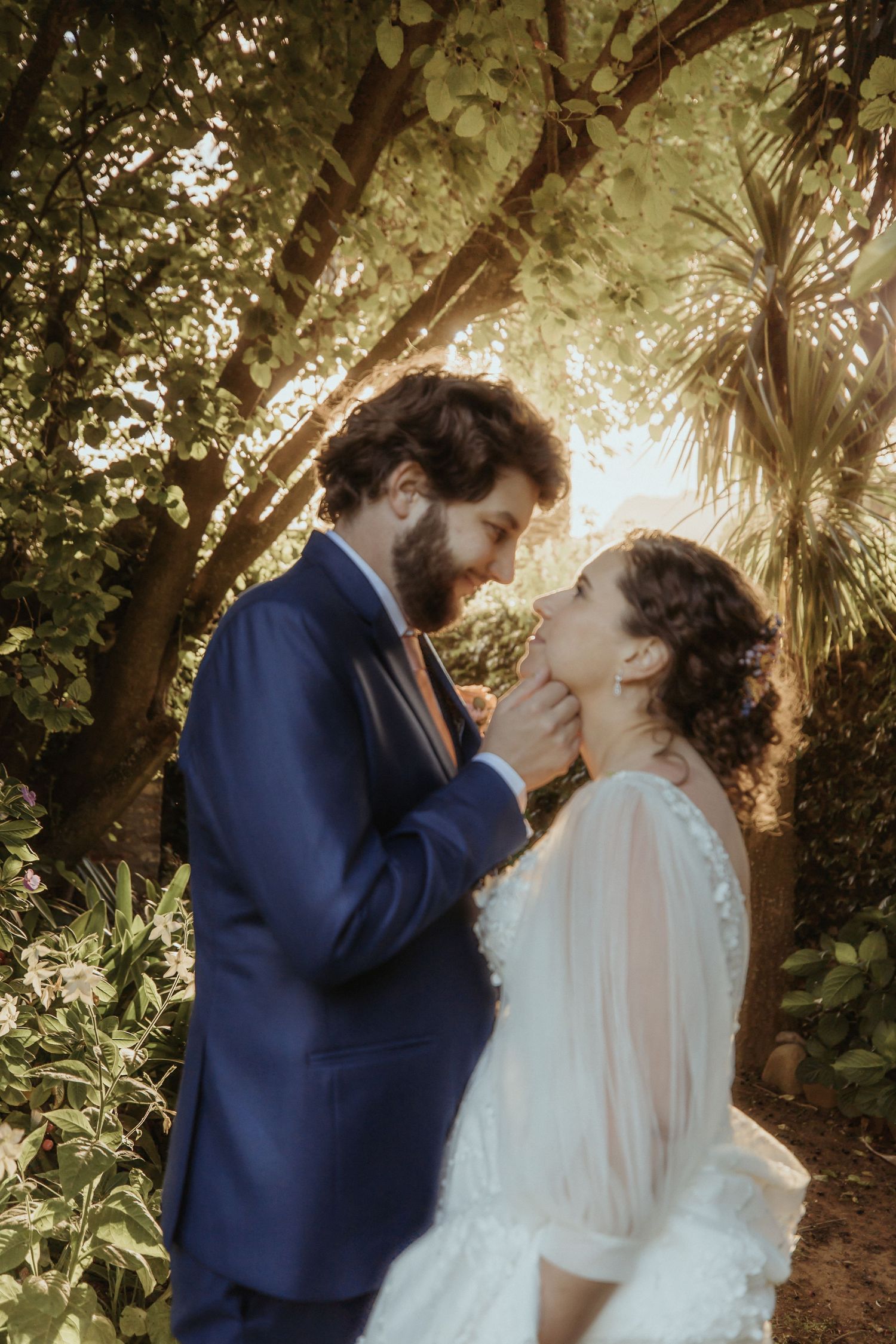 Romantic wedding couple sharing an intimate moment in a sunlit garden setting with lush greenery.