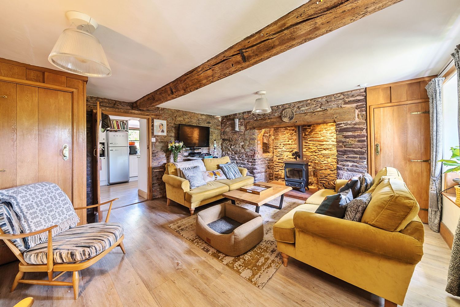 A cozy rustic vacation rental with exposed wooden beams, stone walls, and comfortable yellow couch seating areas.