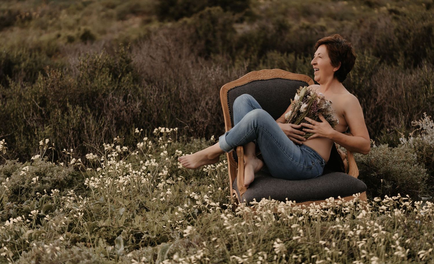 Someone relaxes in a vintage chair among wildflowers while holding a pet cat at golden hour.