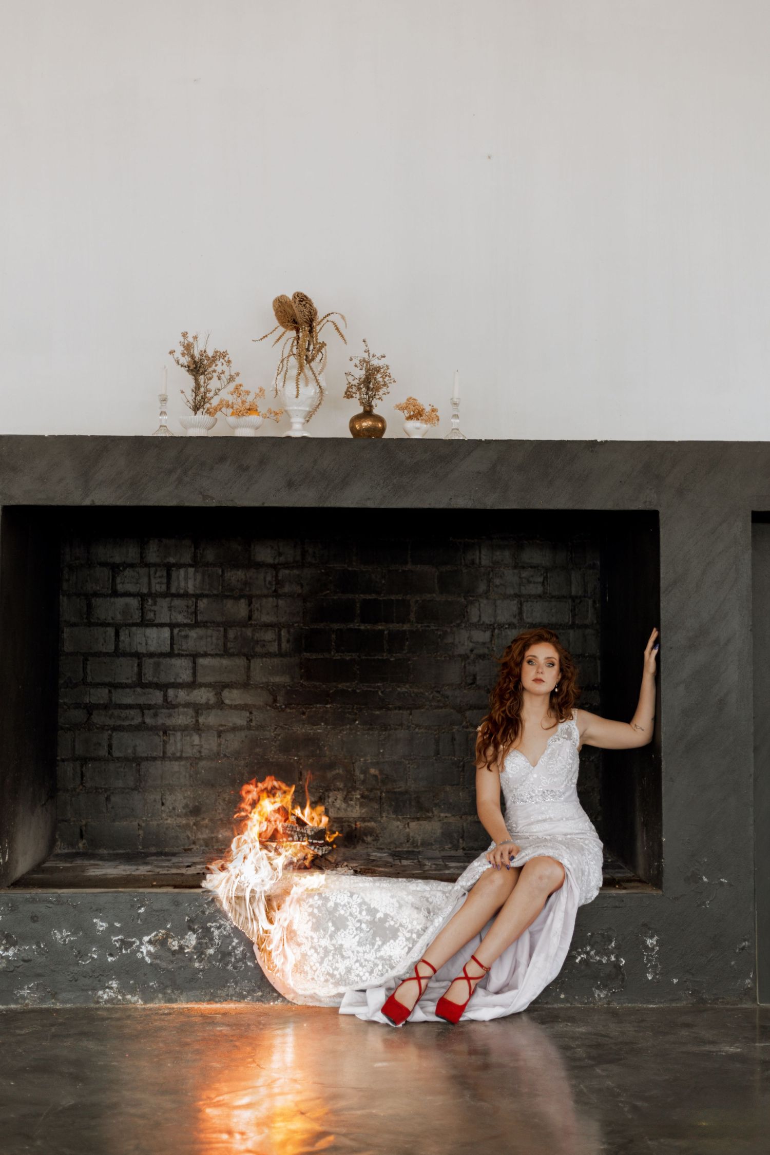 Woman in white dress and red shoes lying on floor as flames dramatically spread across the fabric.