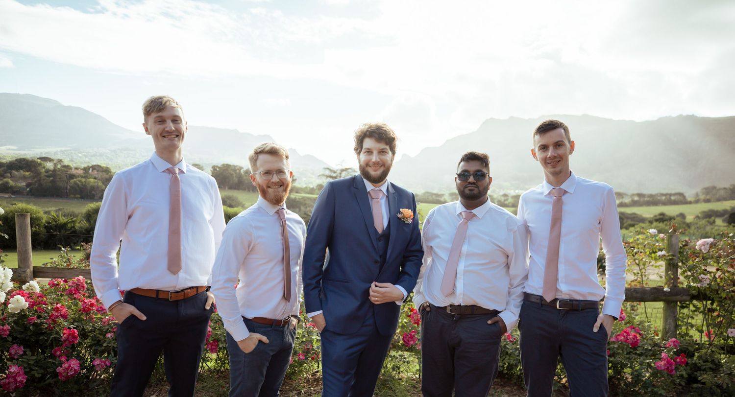 Wedding party members pose outdoors in coordinated blue and white attire with scenic mountain views in the background.