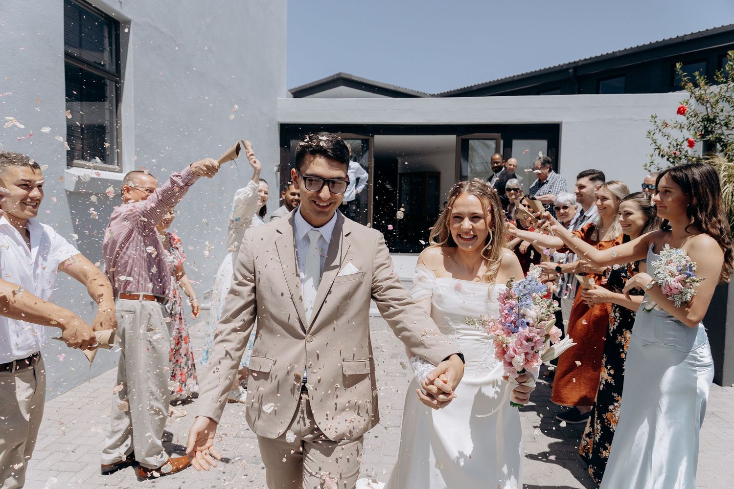 Wedding guests shower newlyweds with flower petals as they exit their ceremony in joyful celebration.