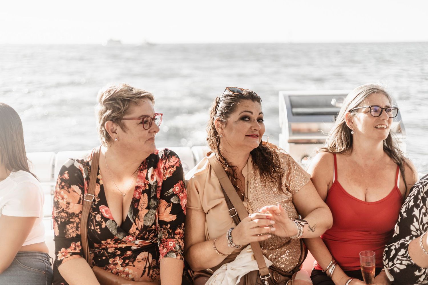 A group of friends in summer outfits sitting together and laughing at the beach on a bright sunny day.