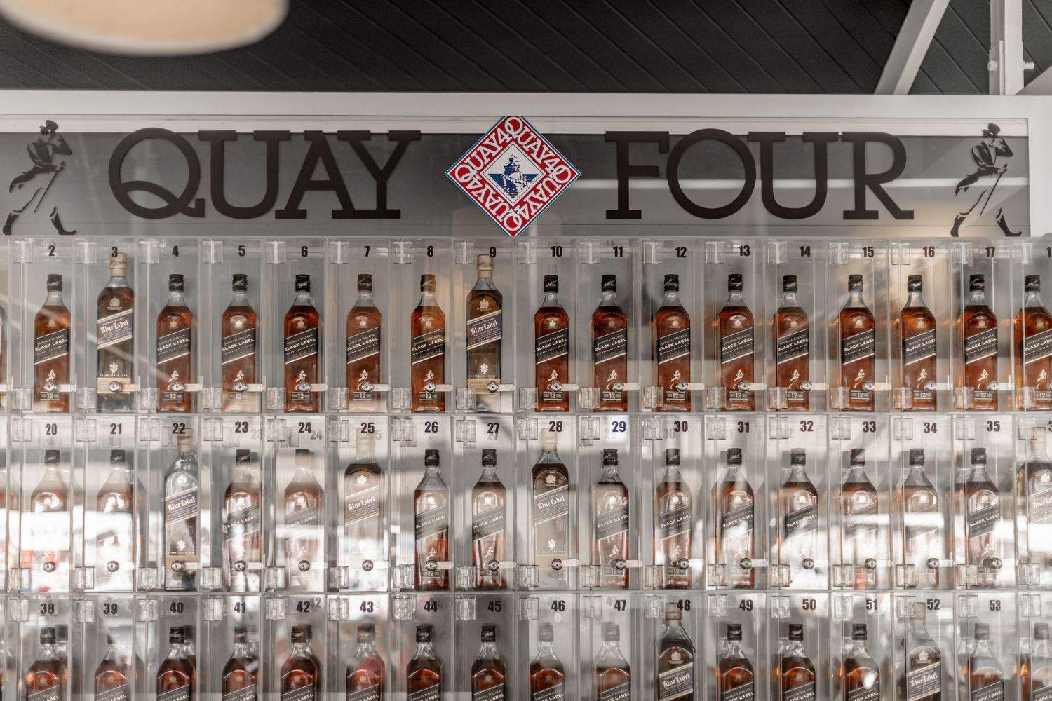 Rows of vodka bottles lined up on illuminated shelves at Quay Four bar display.