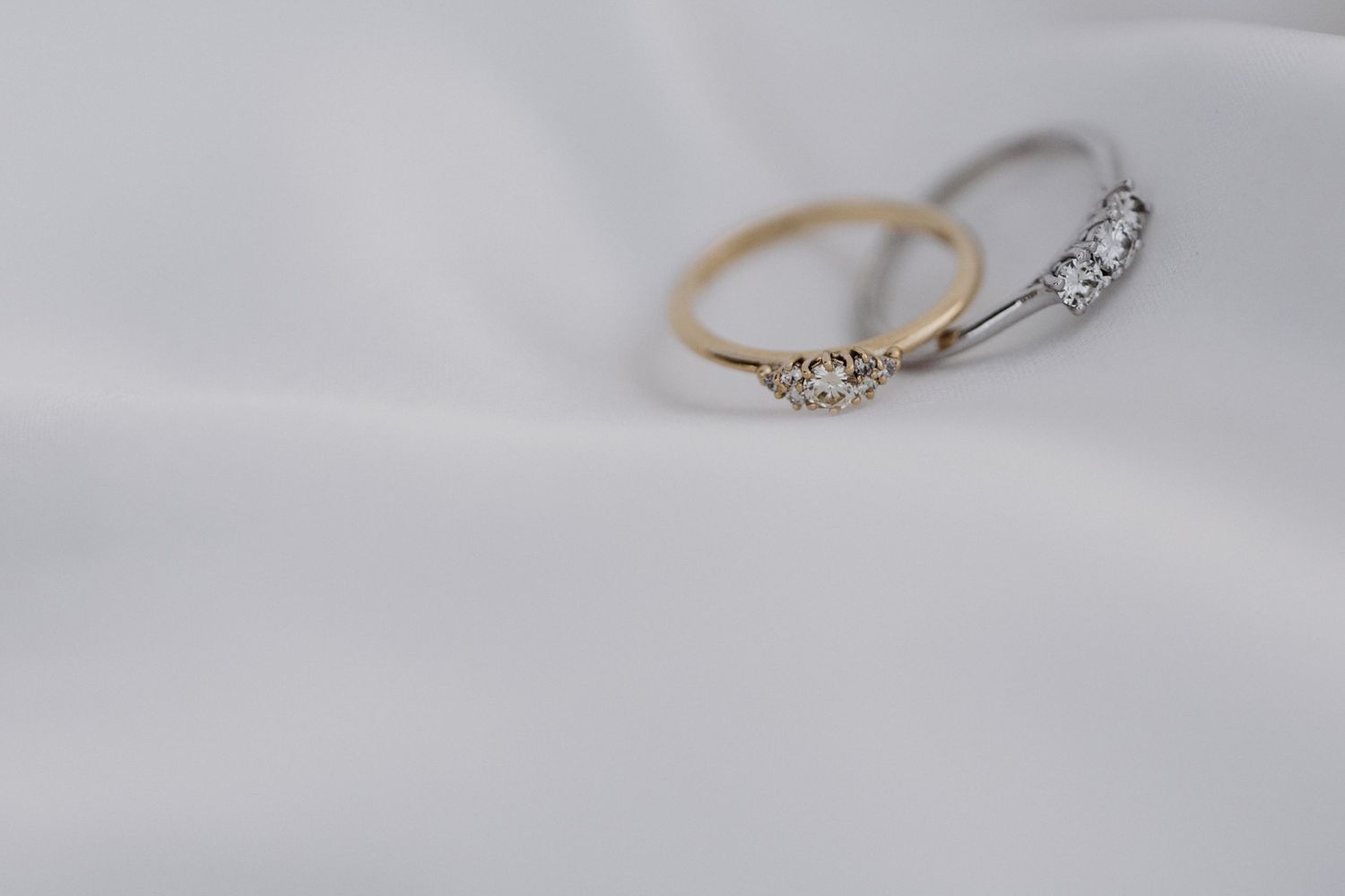 Close up view of delicate diamond rings displayed on a soft white surface showing fine jewelry details.