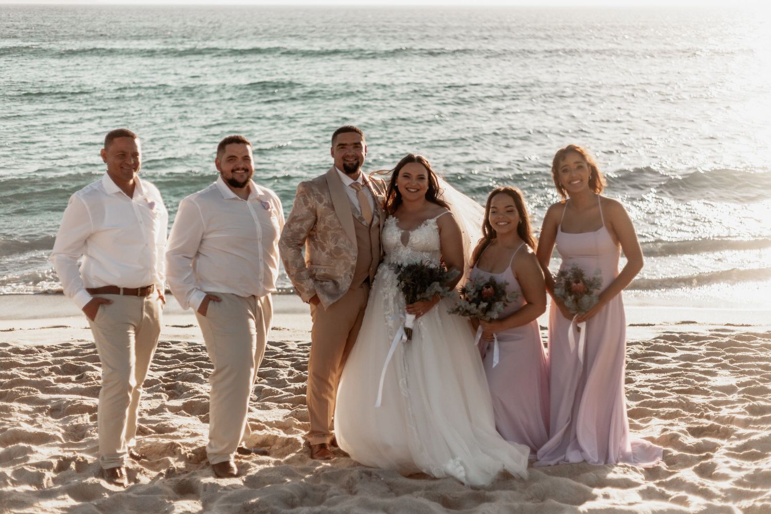 Wedding party walks along sandy beach at sunset during beach ceremony in Florida.