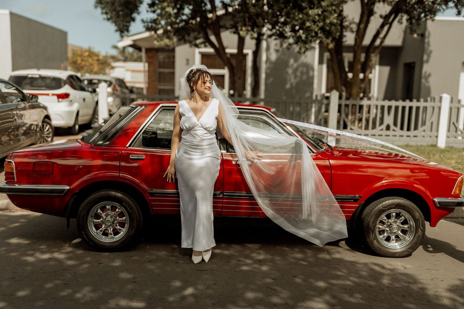 Wedding couple stands next to a classic red car during an outdoor autumn photo session.