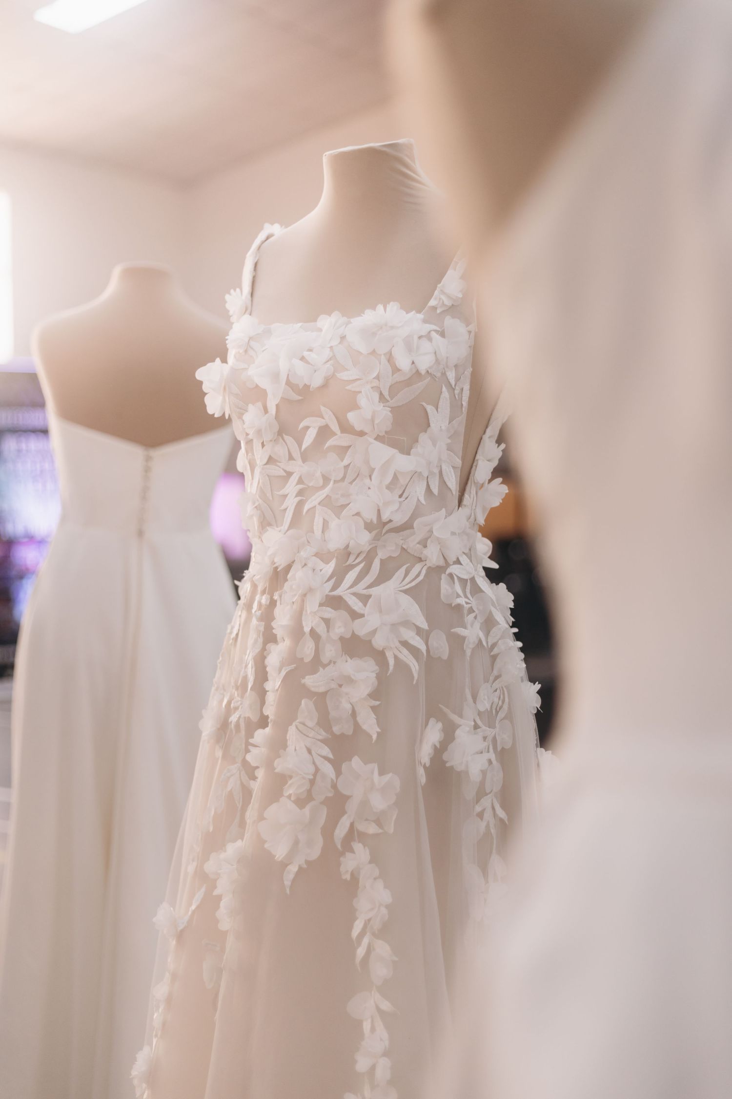 Elegant white bridal gown with 3D floral appliques displayed on a mannequin in a wedding dress boutique.