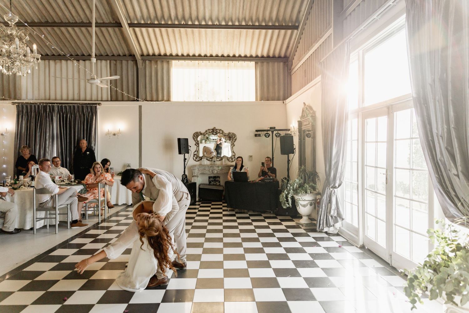 Groom bowing to bride on black and white checkered dance floor at elegant wedding reception.