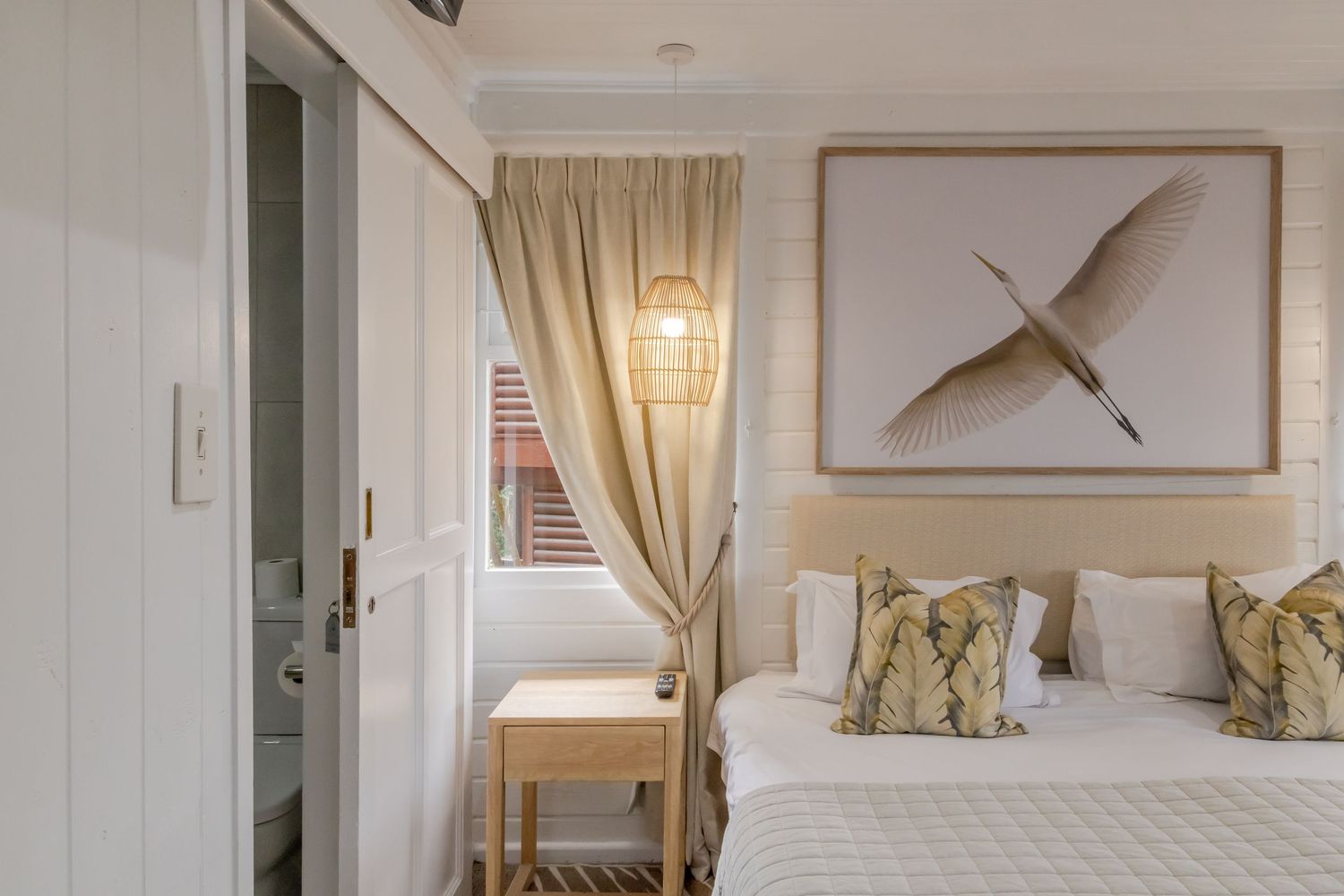 Cozy modern bedroom interior with white bedding, beige curtains, pendant light, and minimalist wall art.