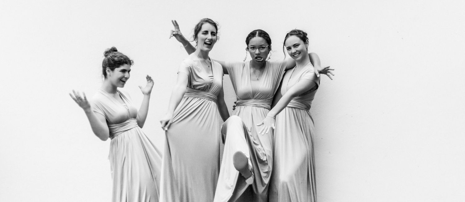 A group in light-colored formal attire poses together on stairs while holding drinks and laughing joyfully.