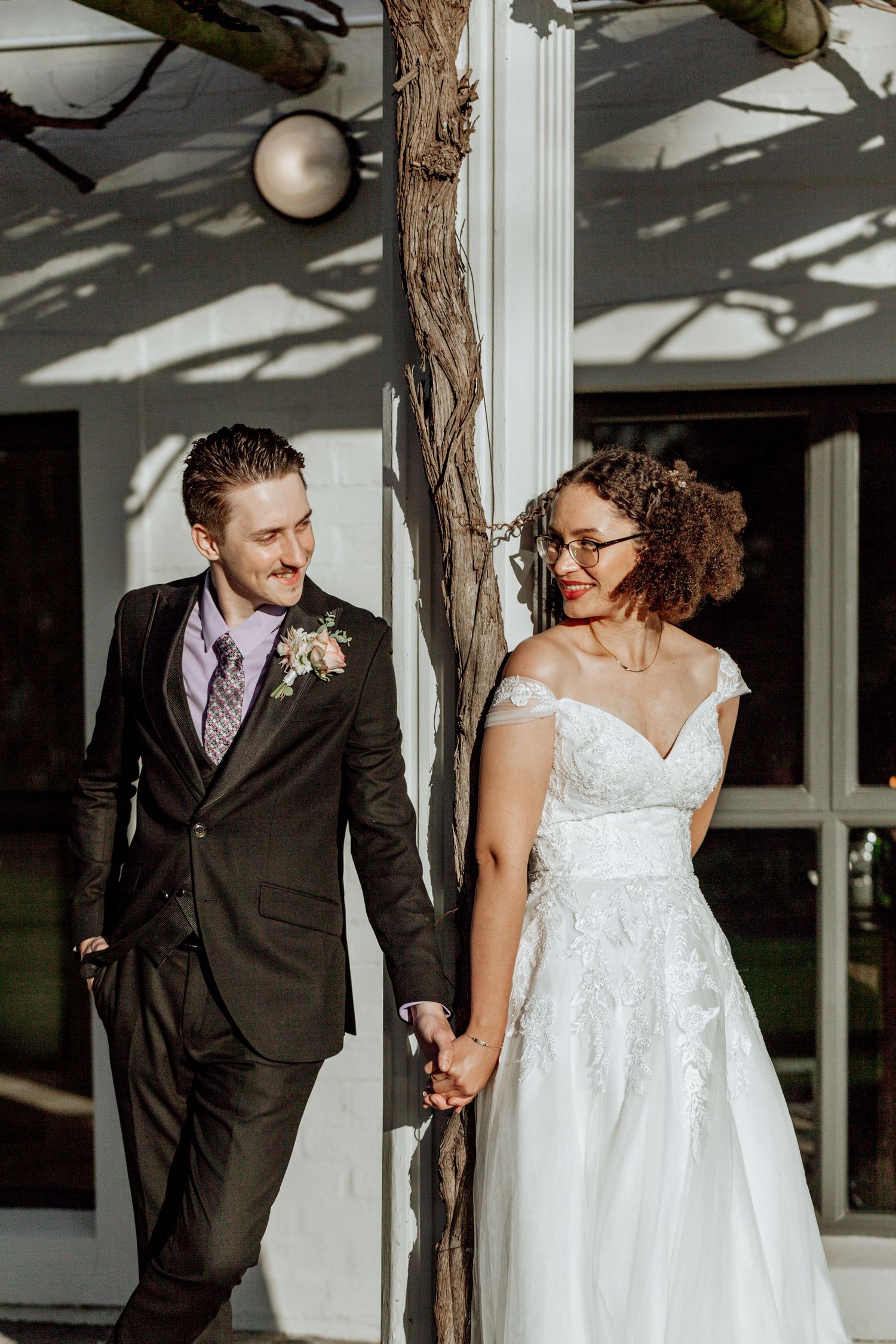 A romantic wedding couple shares laughs and tender moments in a sunlit hallway with natural lighting and wooden beams.