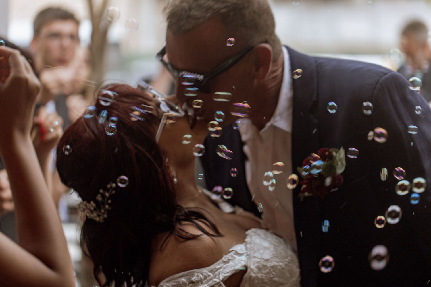 Romantic newlyweds share a tender kiss at their wedding reception while delicate soap bubbles float around them.