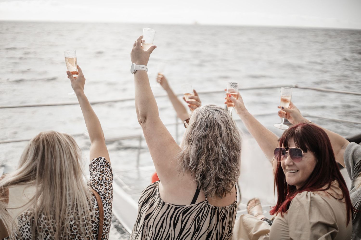 A group of people with raised hands celebrate together on a beach near the water during sunset.