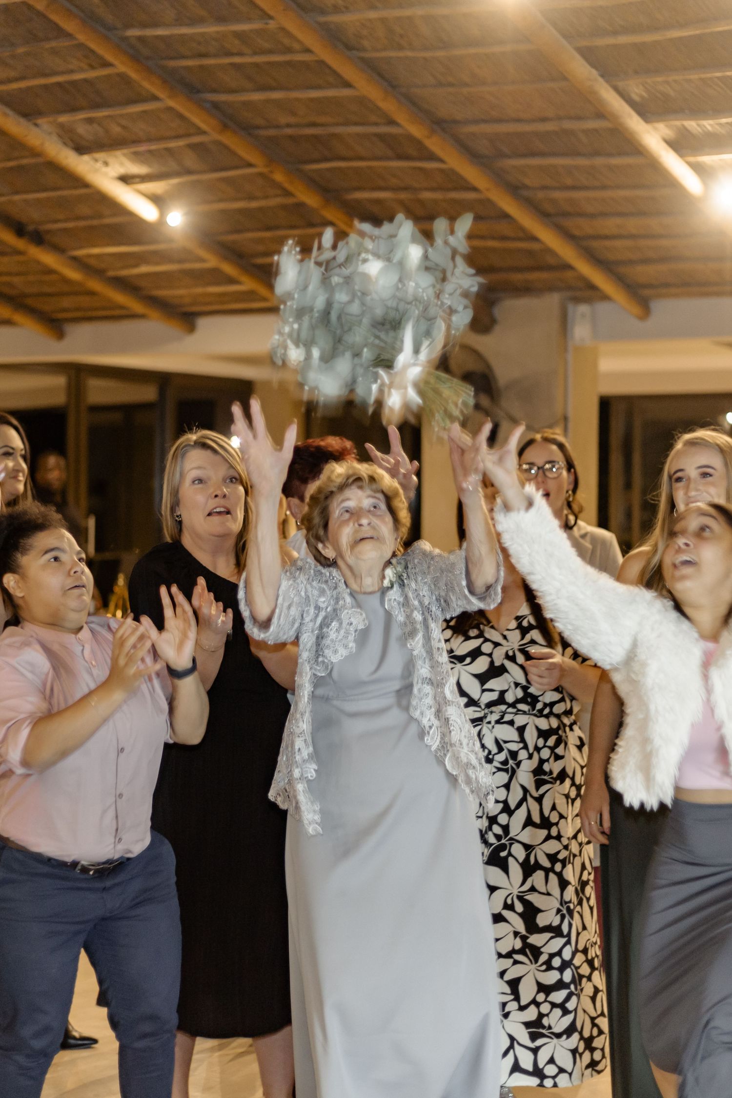 A group of people at an indoor event raise their hands enthusiastically while participating in an activity together.